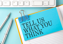 Tell Us What You Think post it note clipped to a stack of papers in front of a computer key board.